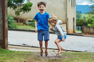 Dzieci w wieku przedszkolnym bawią się i skaczą w błocie.