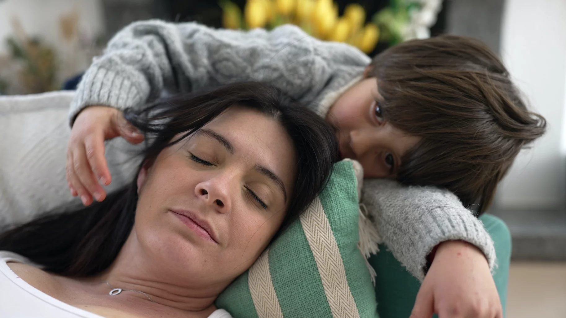 Na zdjęciu mama odpoczywa na kanapie, a dziecko chce ją przytulić.