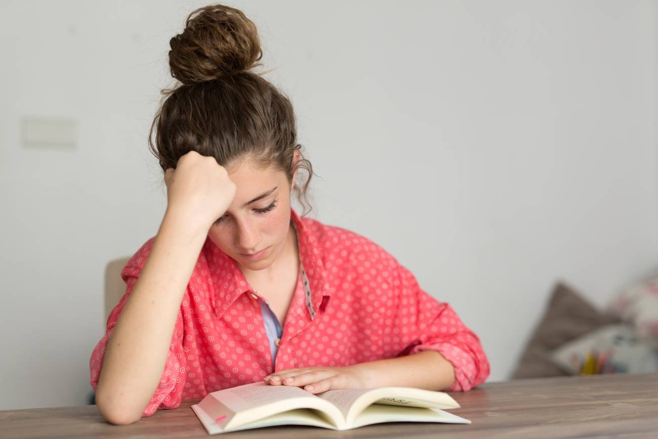 Obrażona nastolatka czyta lekturę szkolną.