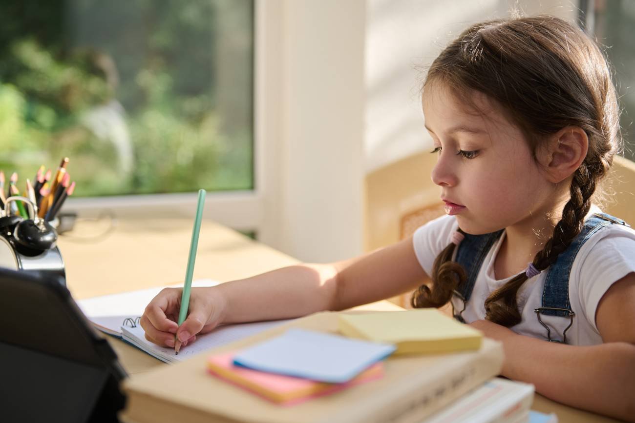 Uczennica pisze w zeszycie wg nowych zasad ortografii.