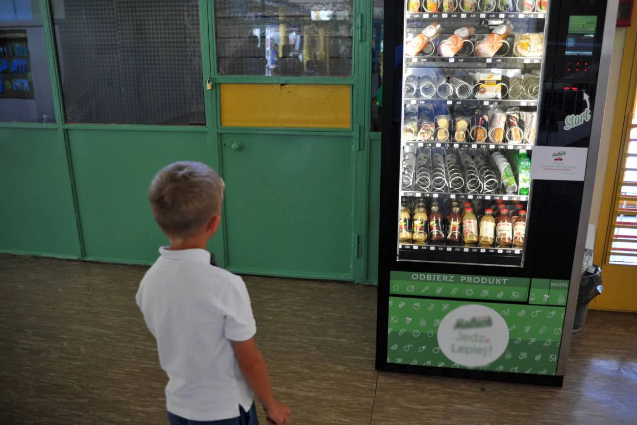 Chłopiec stoi na szkolnym korytarzu przed automatem.
