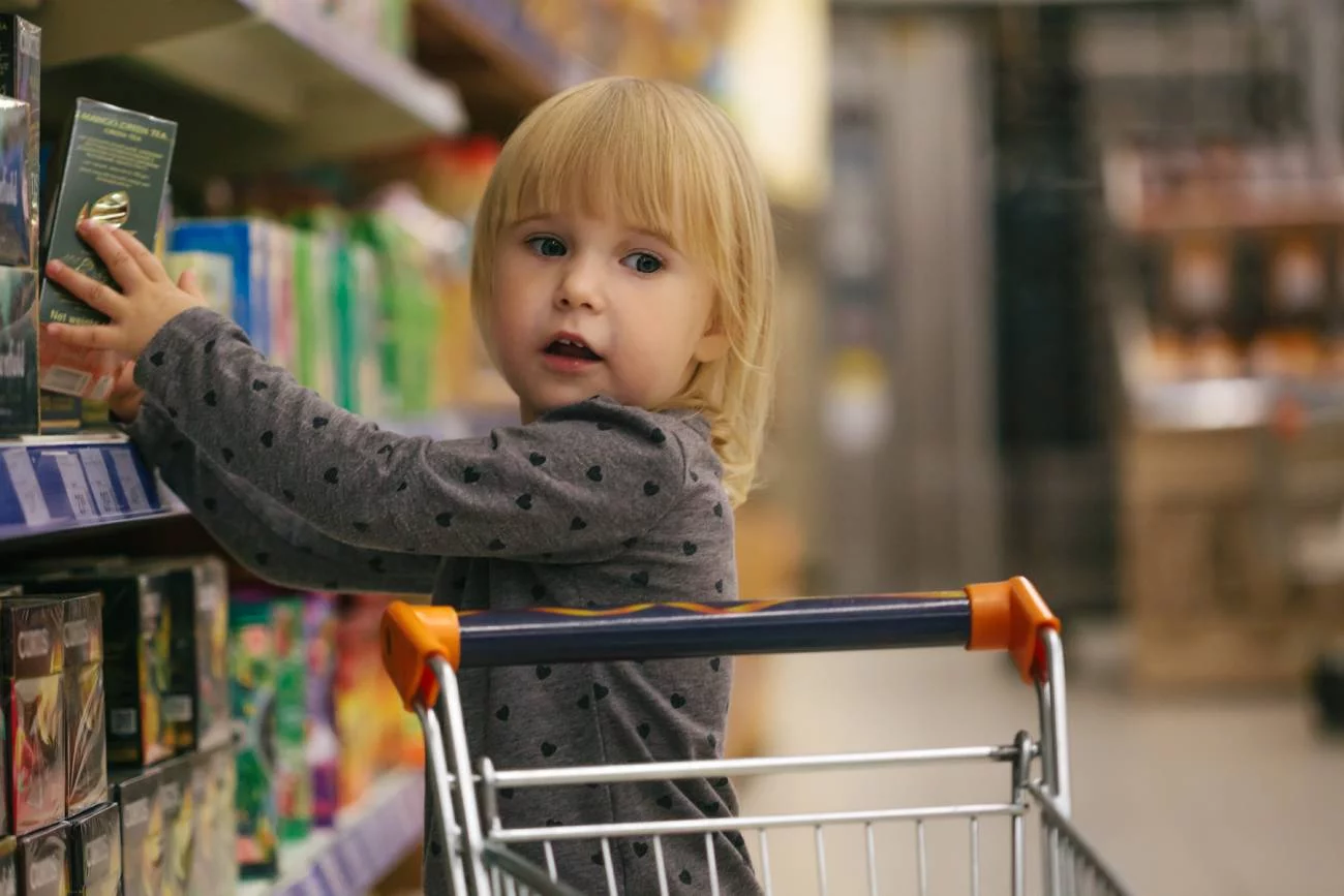Mała dziewczynka na zakupach w markecie wkłada produkty do koszyka.