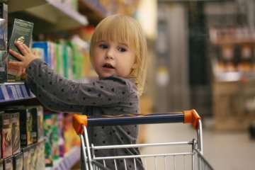 Mała dziewczynka na zakupach w markecie wkłada produkty do koszyka.