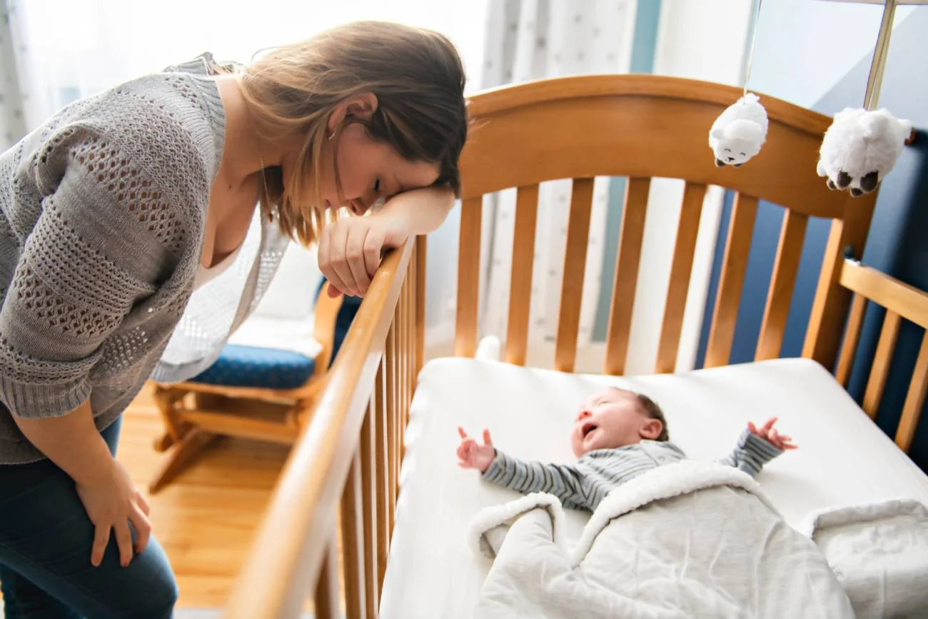 Zmęczona mama nachyla się nad łóżeczkiem niemowlaka. Zmęczona mama nachyla się nad łóżeczkiem niemowlaka.
