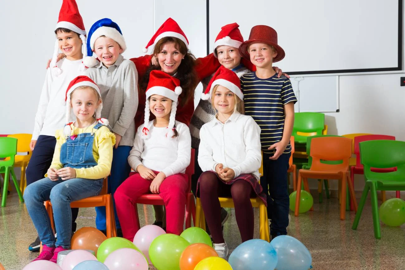 Dzieci w szkole w czapkach mikołajkowych z wychowawczynią.