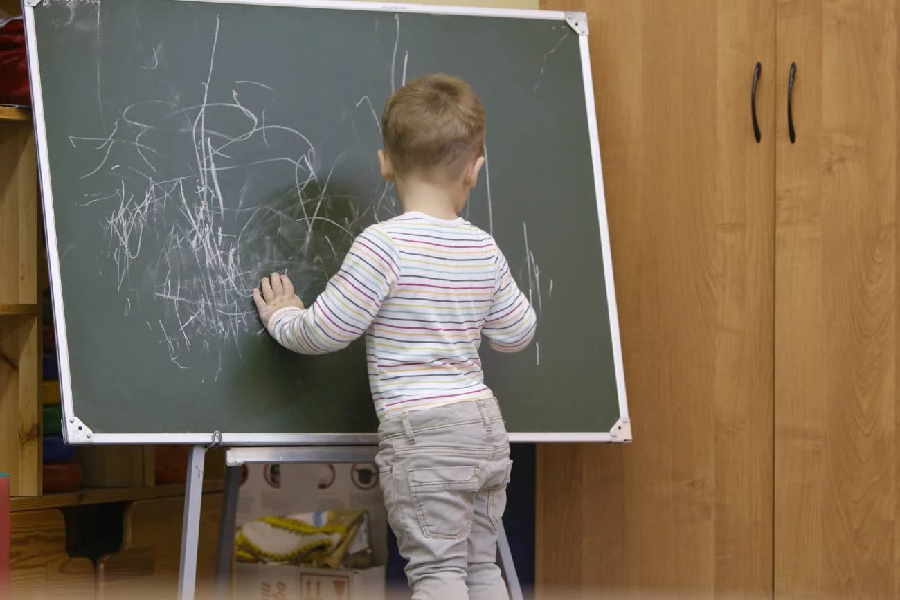 chłopiec w przedszkolnej sali pisze na tablicy