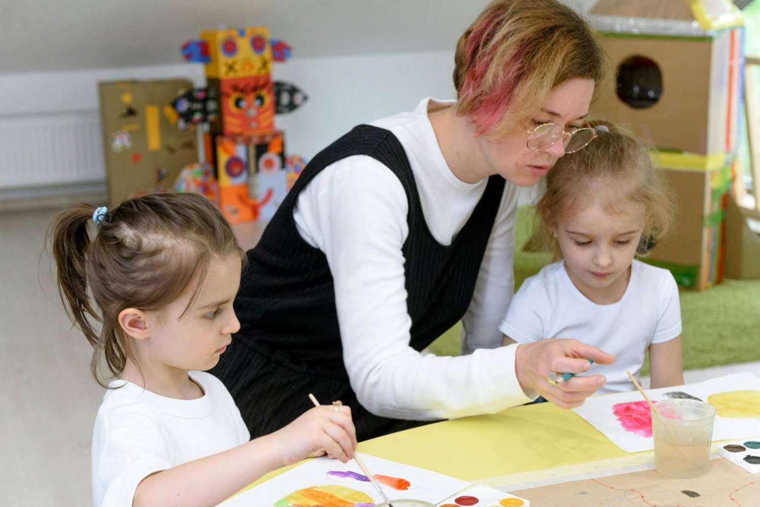 nauczycielka w przedszkolu z dziećmi pracuje przy stolikach