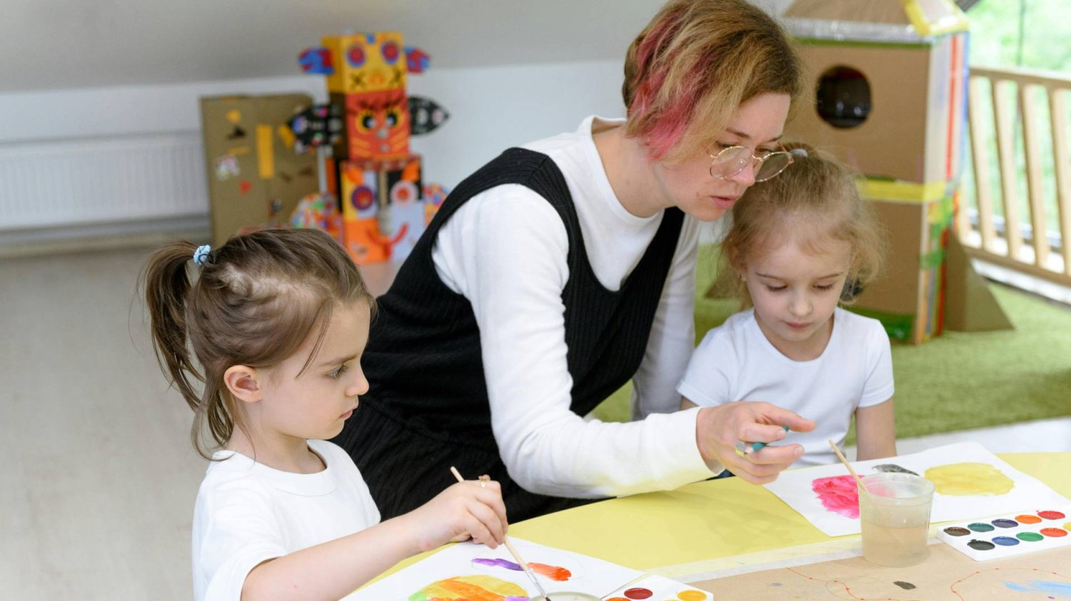 nauczycielka w przedszkolu z dziećmi pracuje przy stolikach