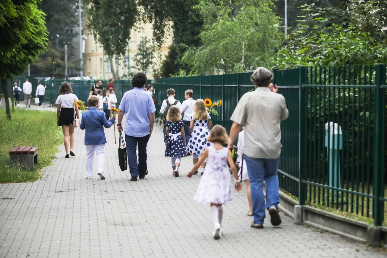 Uczniowie idą z rodzicami na zakończenie roku szkolnego.