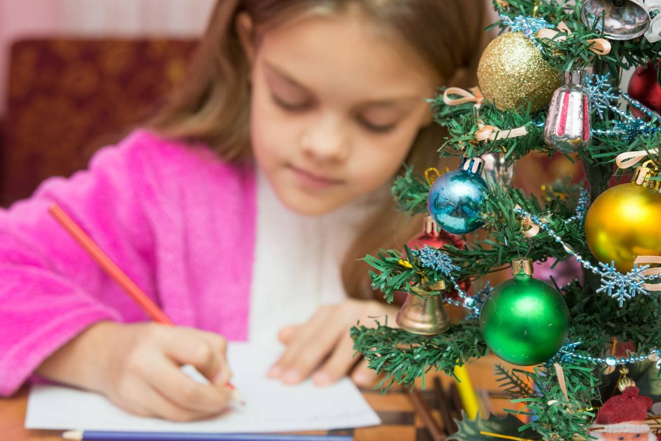 Dziewczynka w wieku szkolnym pisze list do św. Mikołaja przy choince.