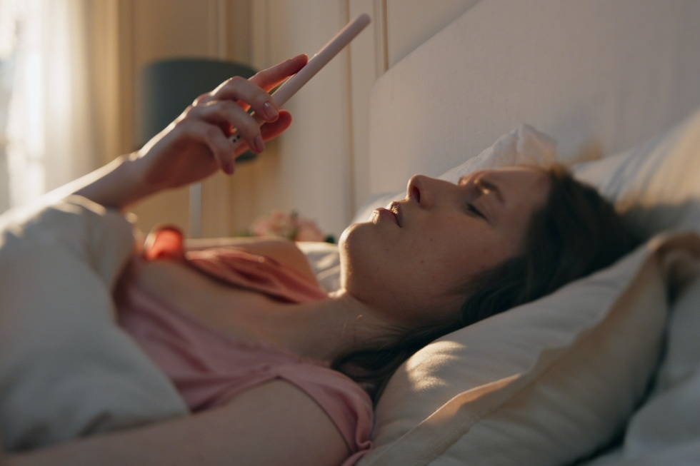 Na zdjęciu widać kobietę, która sprawdza telefon w łóżku po przebudzeniu