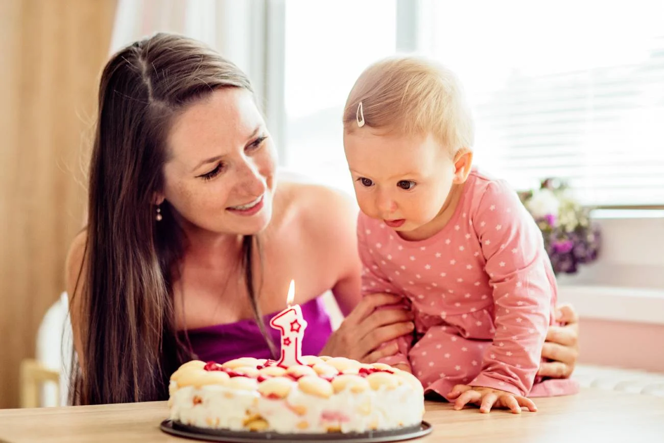 Mama z córką dmuchają świeczkę na torcie z okazji 1. urodzin.