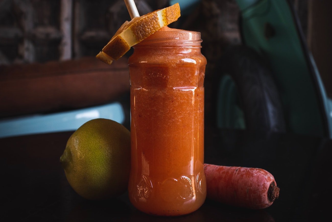 Słoik z sokiem marchwiowym i słomką.
