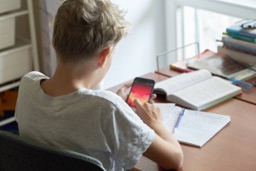 Uczeń patrzy w smartfona, zamiast odrabiać lekcje. Uczeń patrzy w smartfona, zamiast odrabiać lekcje.