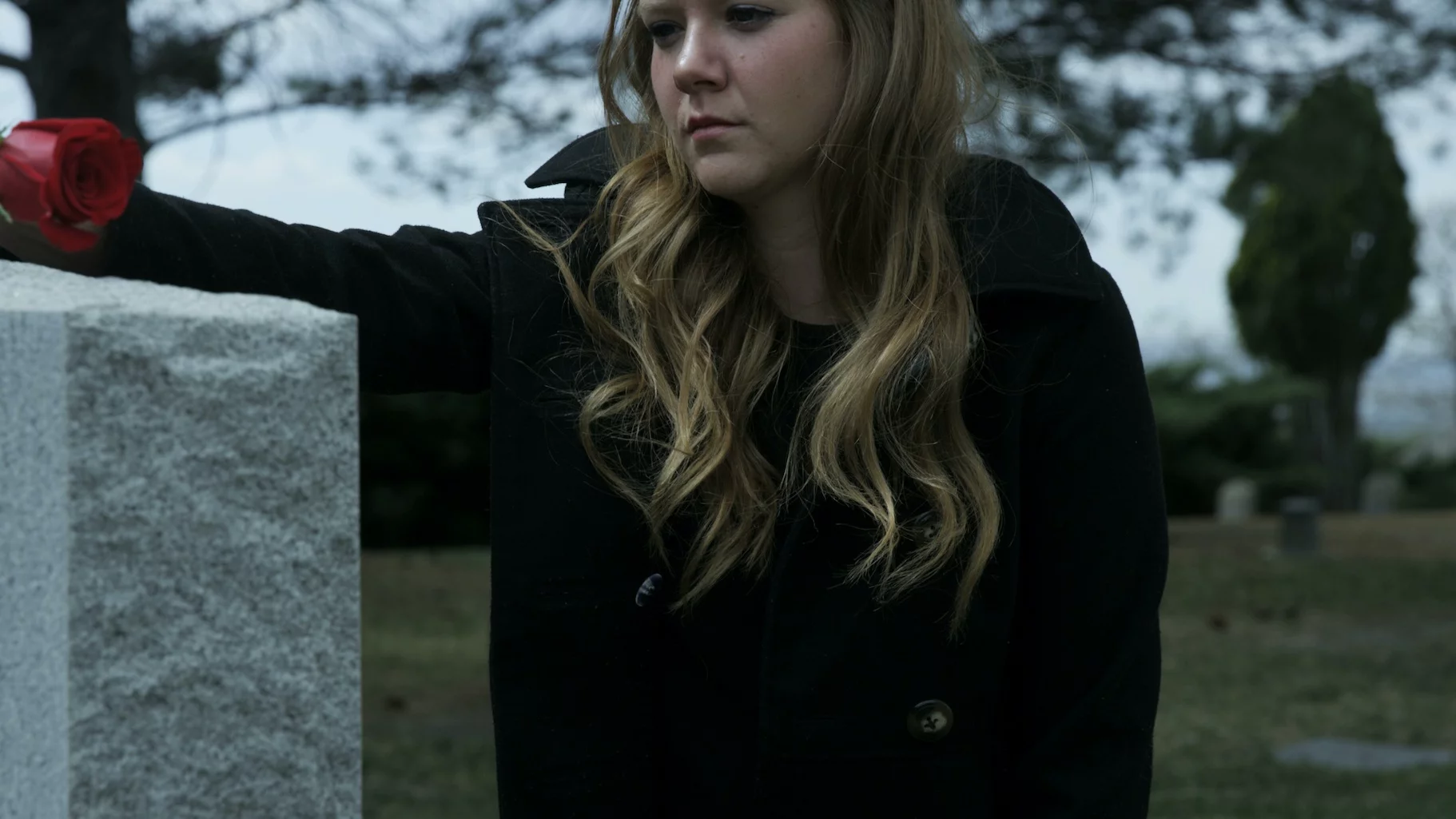 Czy zabierać dziecko na cmentarz na wszystkich świętych? Na zdjęciu młoda kobieta kładzie różę na grobie bliskiej osoby