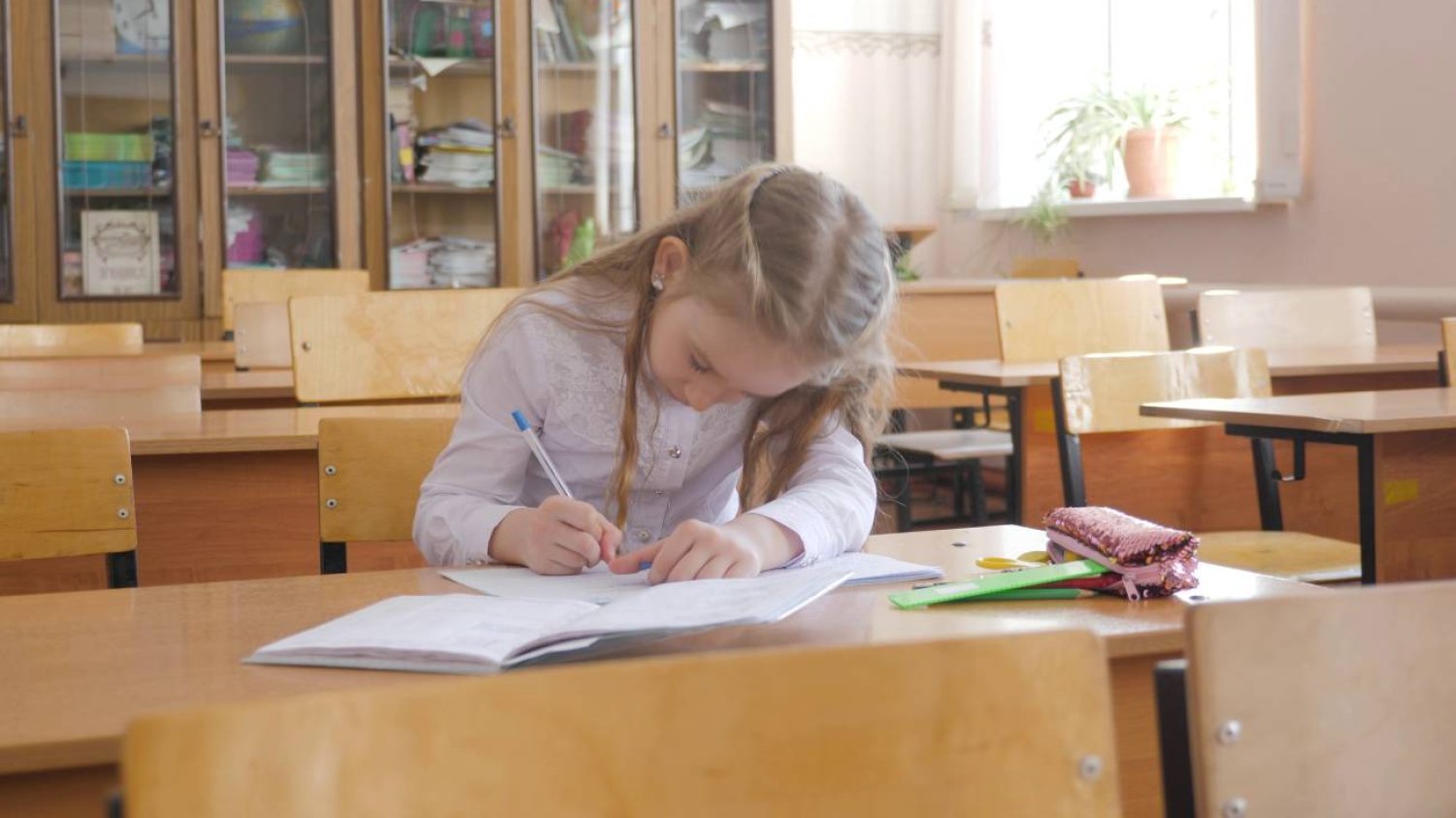 dziewczynka siedzi w szkolnej ławce i pisze w zeszycie dziewczynka siedzi w szkolnej ławce i pisze w zeszycie