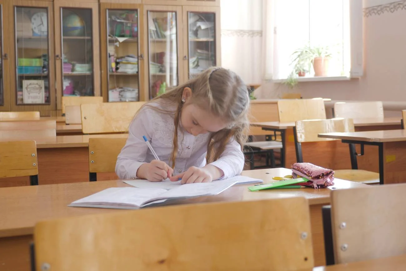 dziewczynka siedzi w szkolnej ławce i pisze w zeszycie