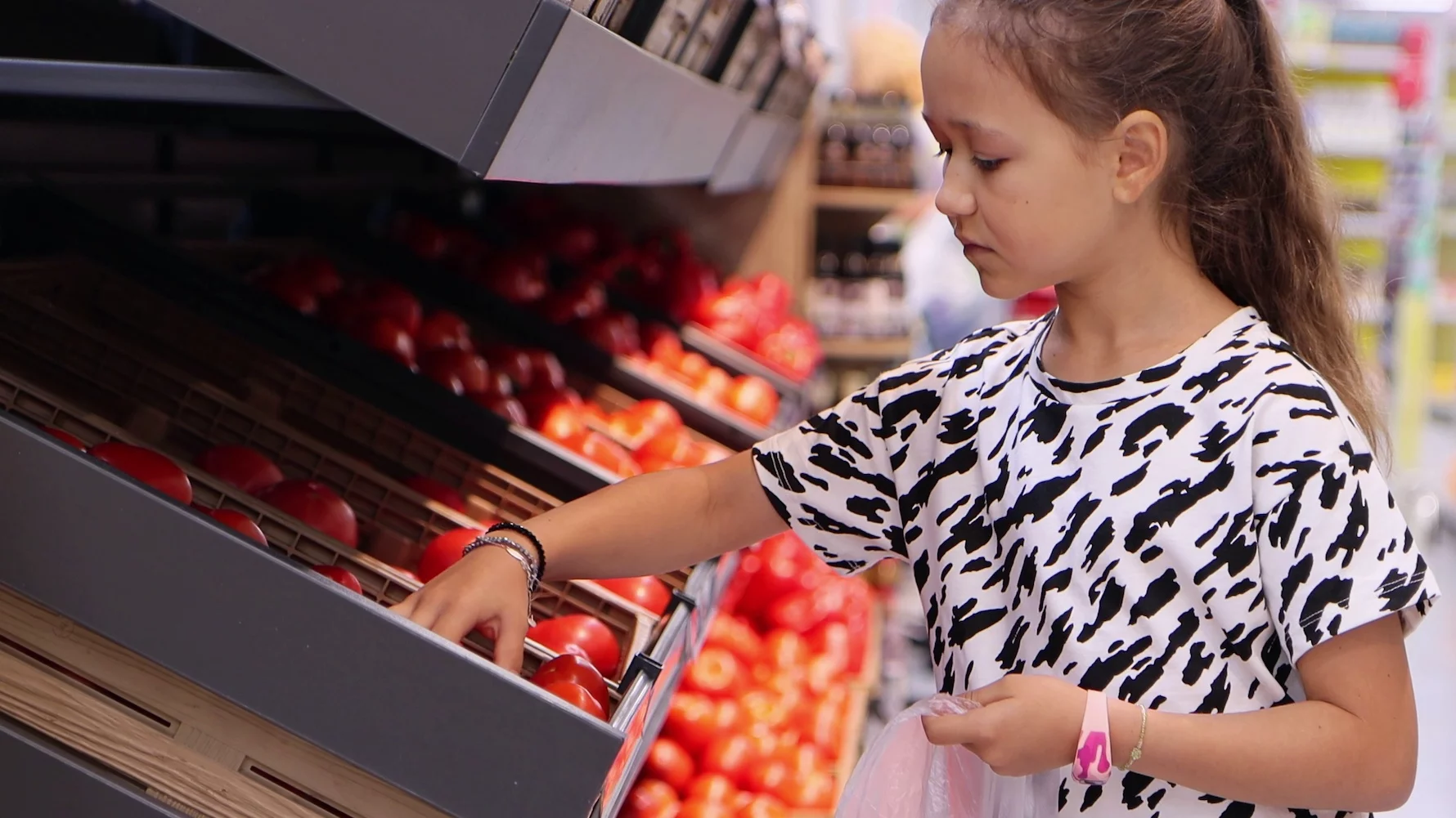 Dziewczynka w supermarkecie wybiera warzywa i owoce.