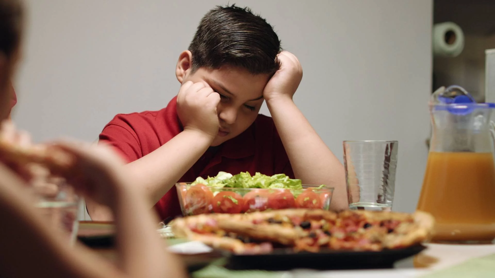 zniechęcony chłopak patrzy się w talerz z niedokończonym posiłkiem zniechęcony chłopak patrzy się w talerz z niedokończonym posiłkiem