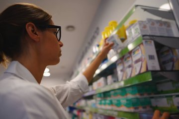 kobieta sprawdza lekarstwa na półce w aptece