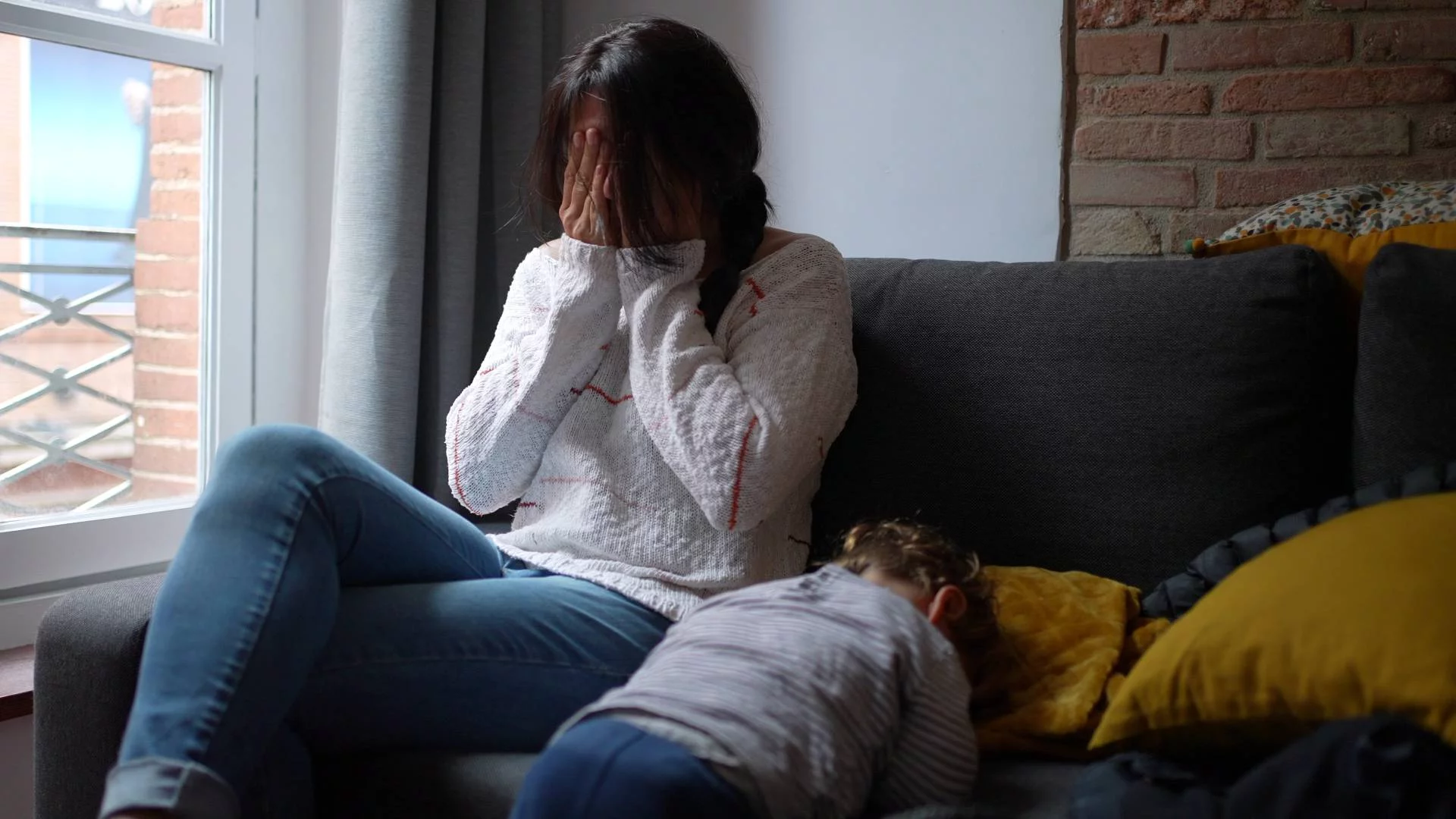 zmęczona mama siedzi na kanapie z dzieckiem i chowa twarz w dłoniach zmęczona mama siedzi na kanapie z dzieckiem i chowa twarz w dłoniach