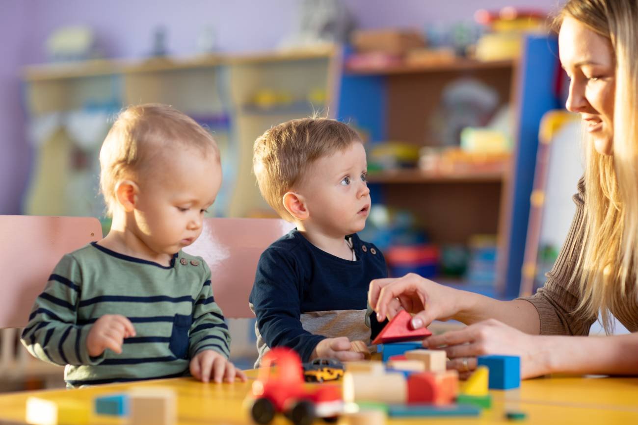 Małe dzieci bawią się w żłobku z opiekunką.