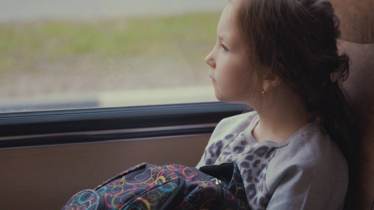 Zmęczona dziewczynka wygląda za okno, jadąc autobusem.