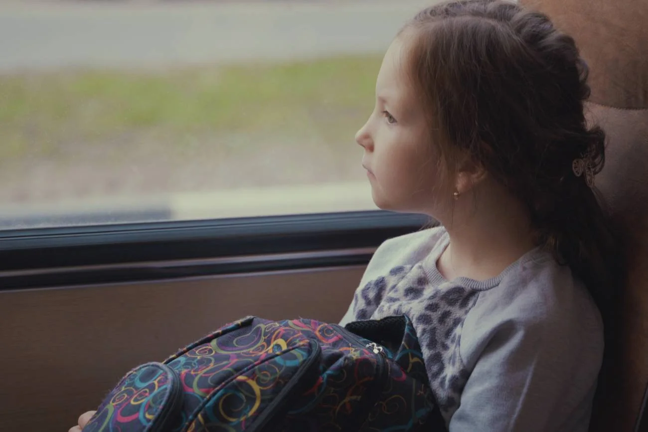 Zmęczona dziewczynka wygląda za okno, jadąc autobusem.