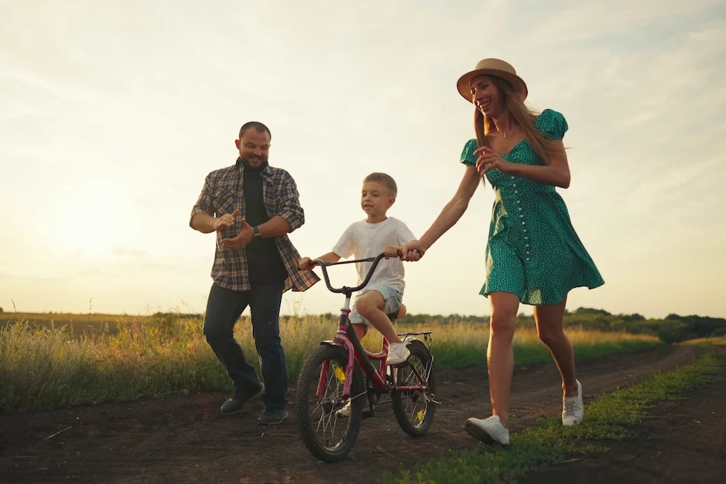 Dziecko uczy się jeździć na rowerze, a rodzice go asekurują.
