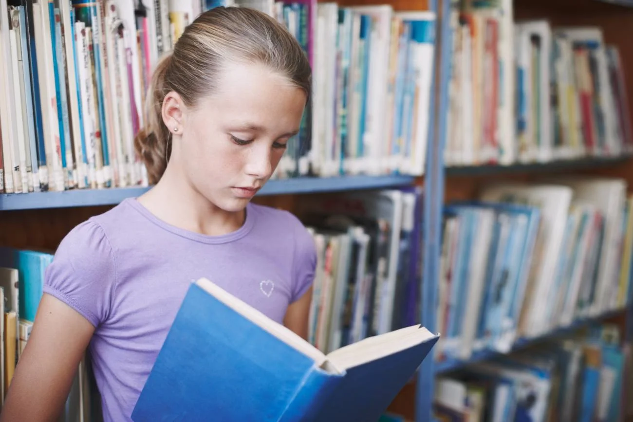 Uczennica czyta lekturę szkolną w bibliotece.