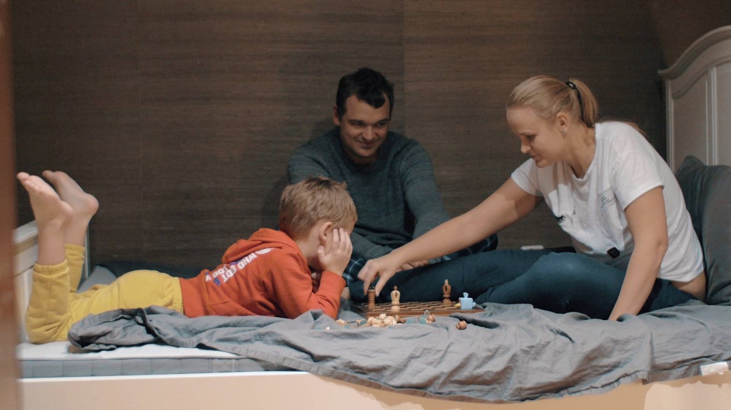 rodzice bawią się z synem, grają wspólnie w szachy na łóżku