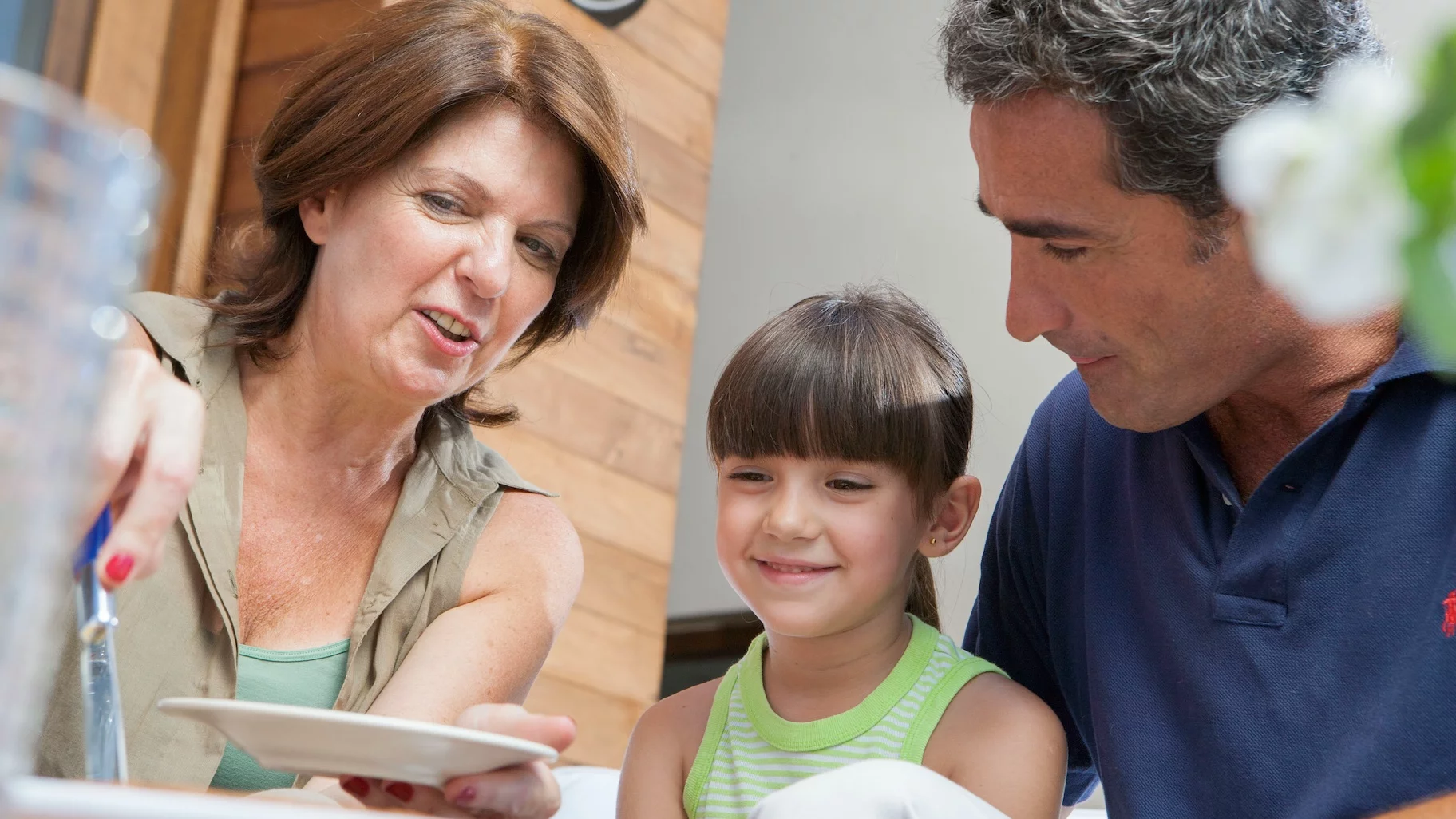 Dziadkowie nie stosują się do zasad rodziców – jak reagować? Na zdjęciu dziadkowie nakładają wnuczce kolejną porcję ciasta