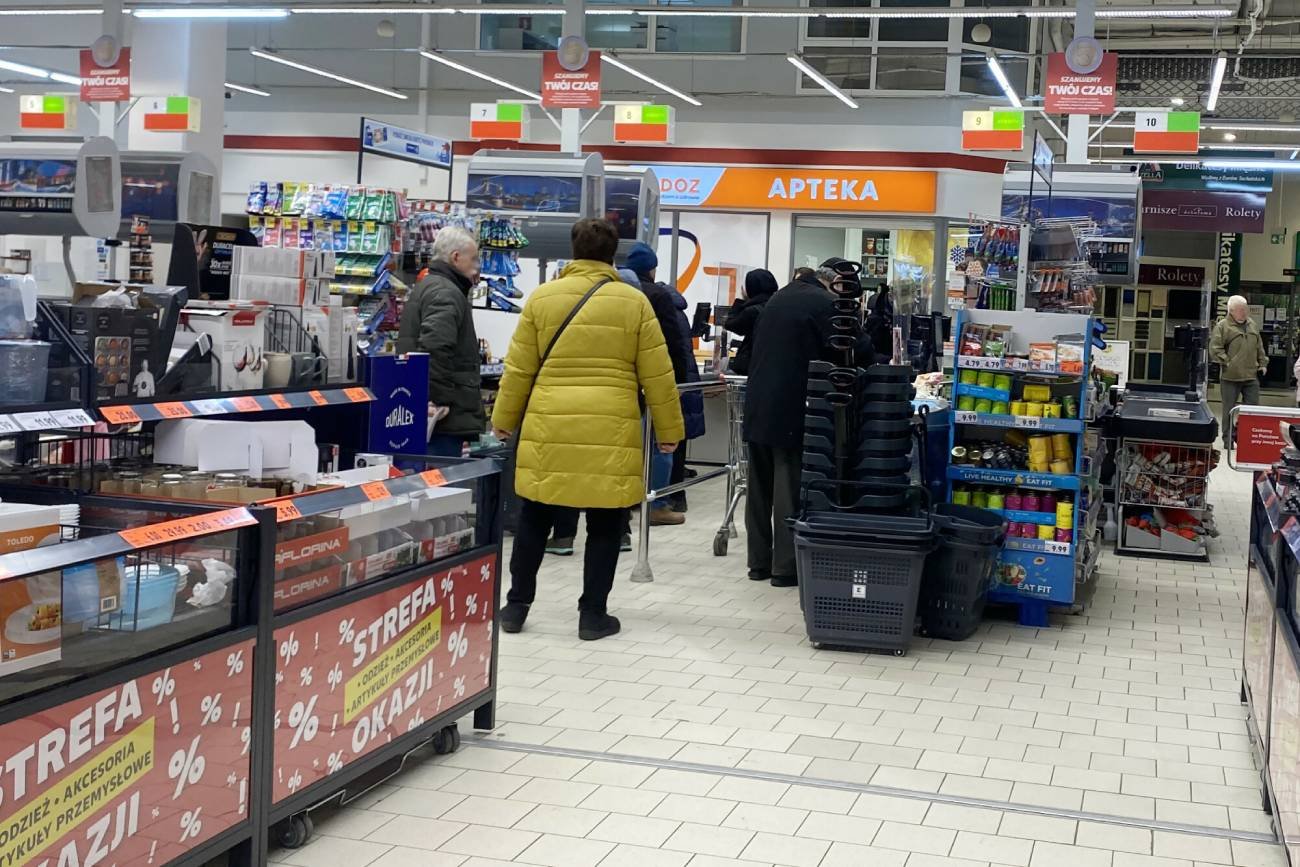 Kolejka w markecie do kasy, przy której jest stoisko z lekarstwami.