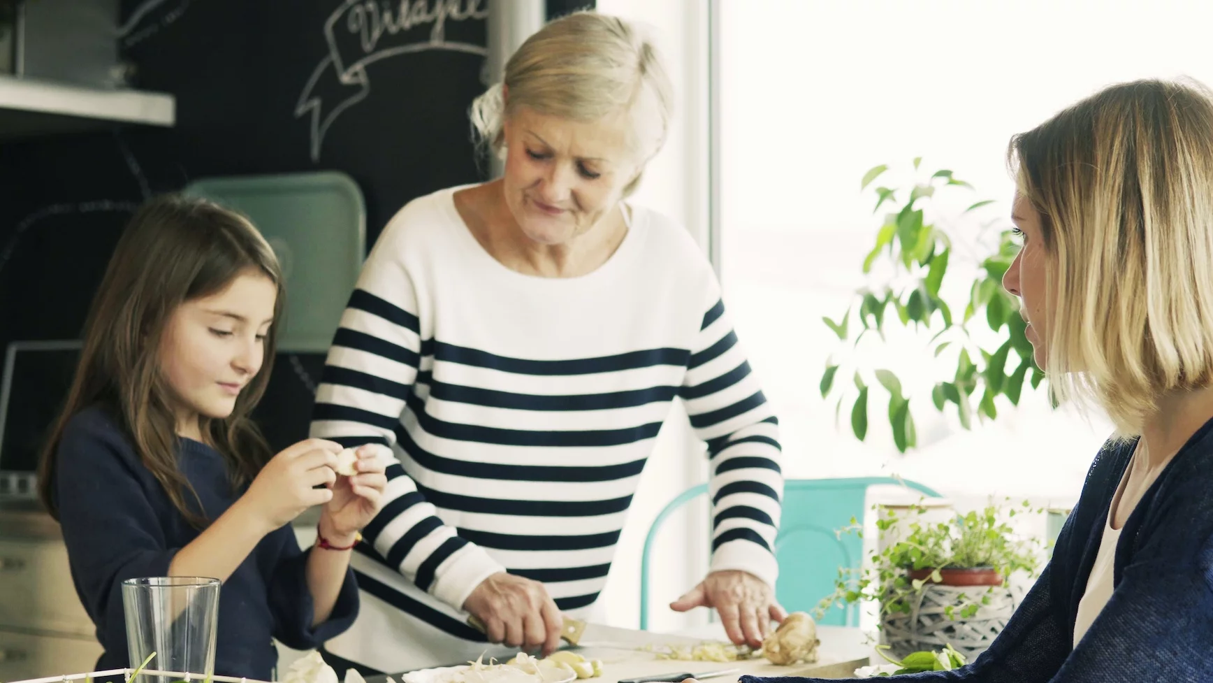 Na zdjęciu babcia z wnuczką przygotowują posiłek. Wszystkiemu przygląda się mama dziewczynki.