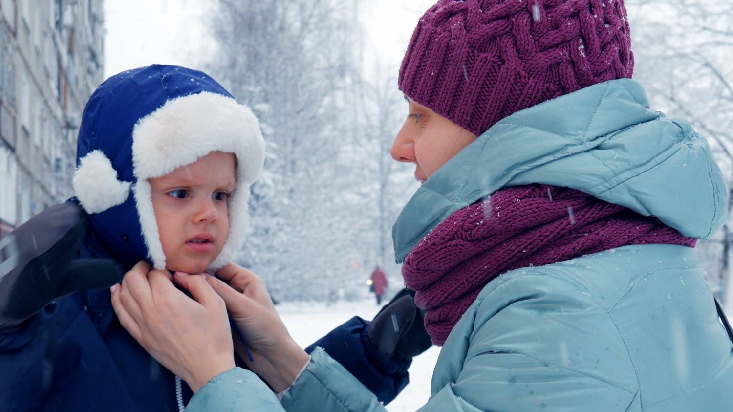 mama na śniegu z dzieckiem, poprawia mu czapkę