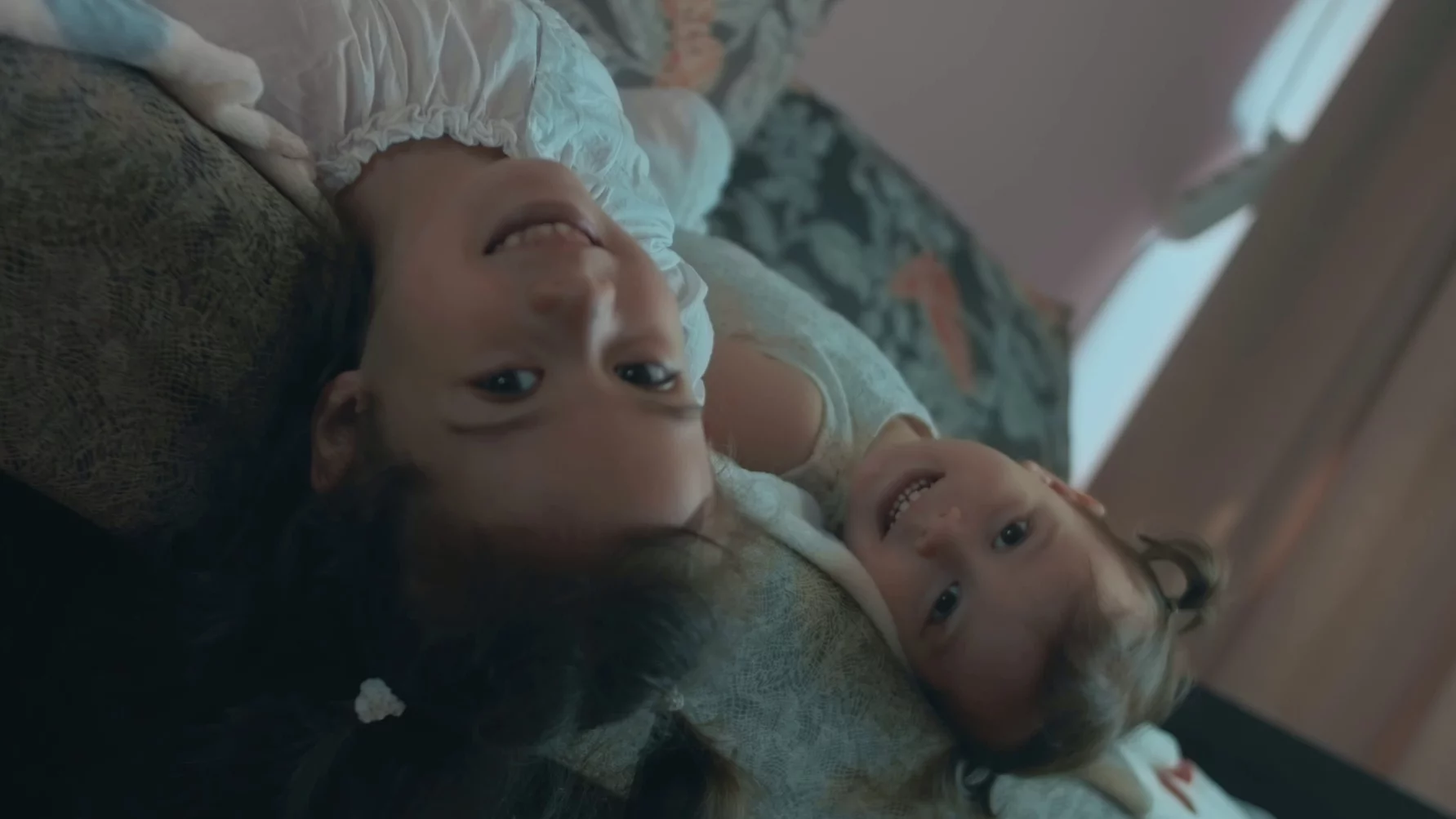 Na zdjęciu dwie dziewczynki w podobnym wieku leżą na kanapie i się wygłupiają