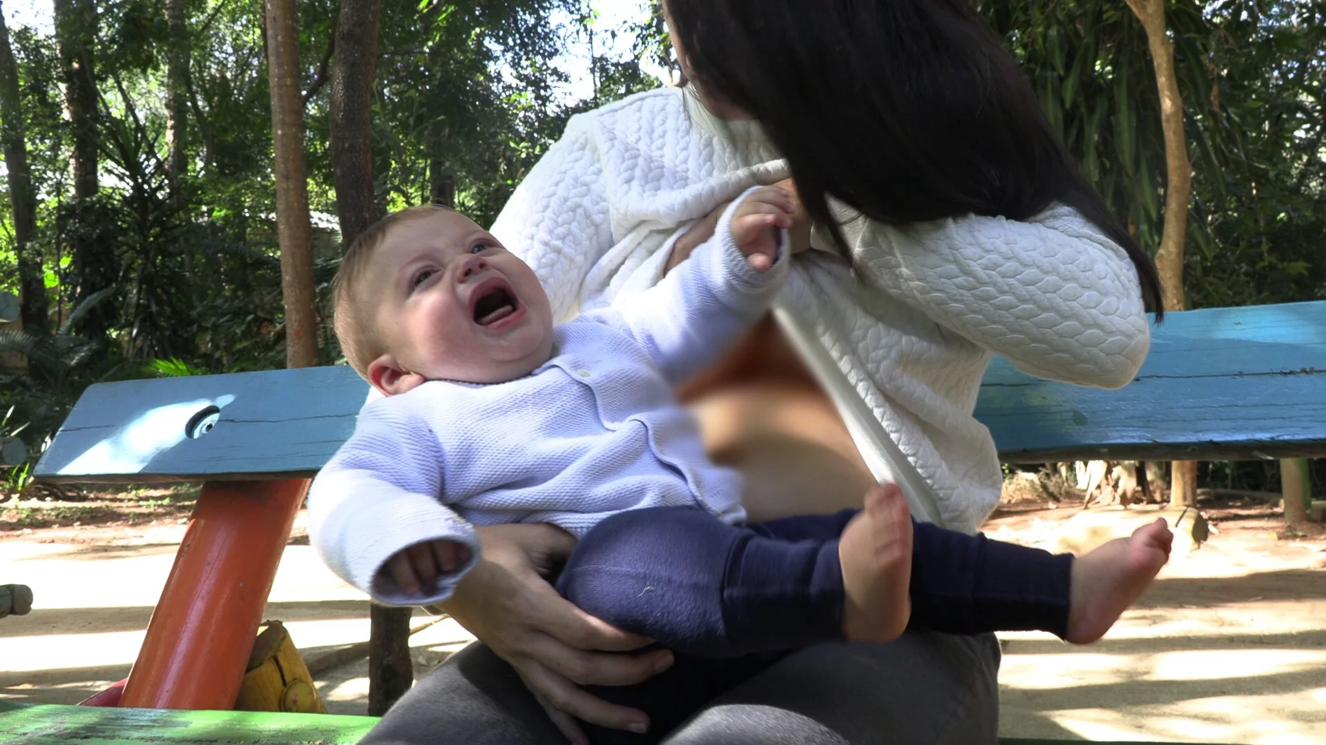 Na zdjęciu widać mamę karmiącą w parku i płaczące niemowlę