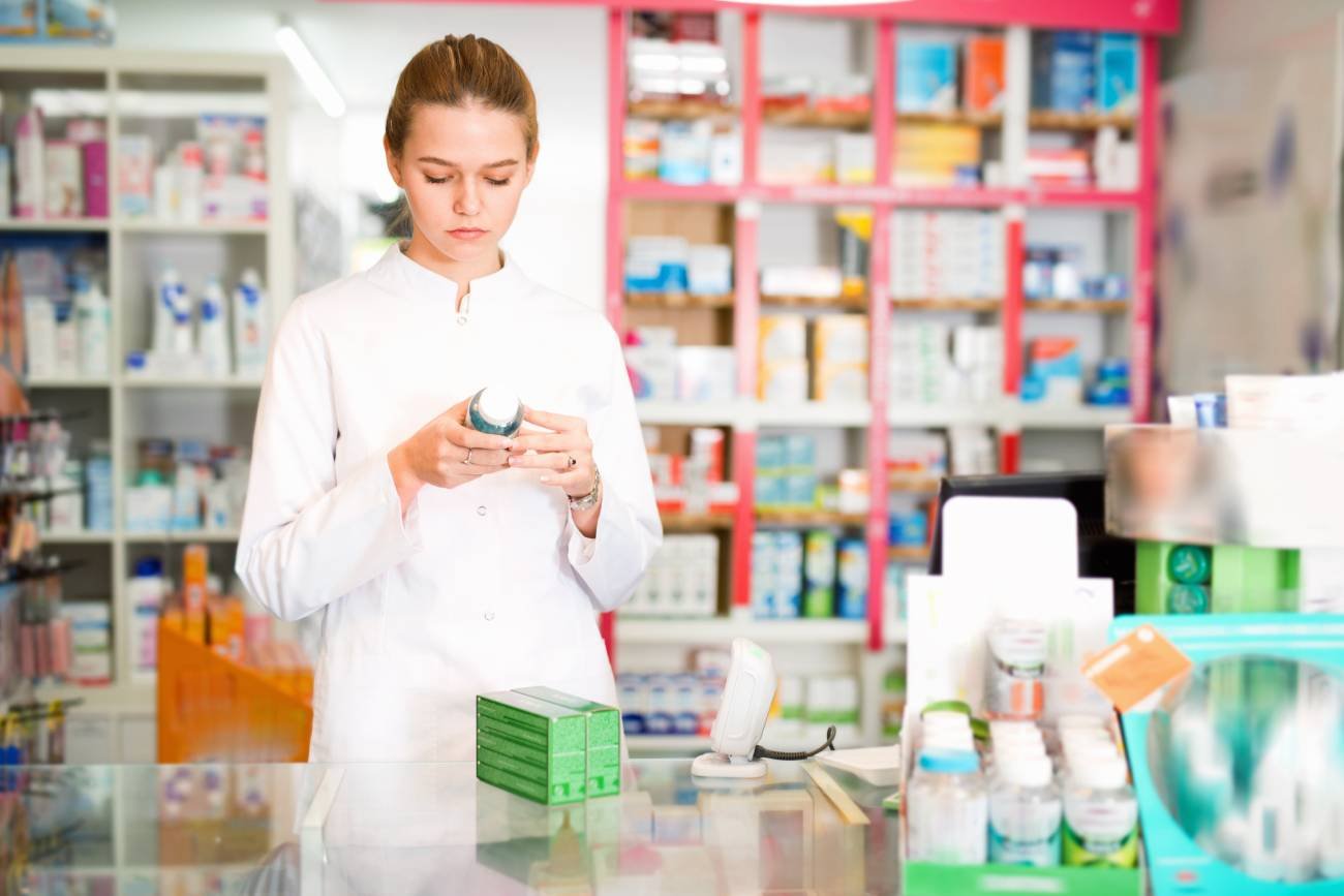 Farmaceutka w aptece czyta opakowanie z lekiem.