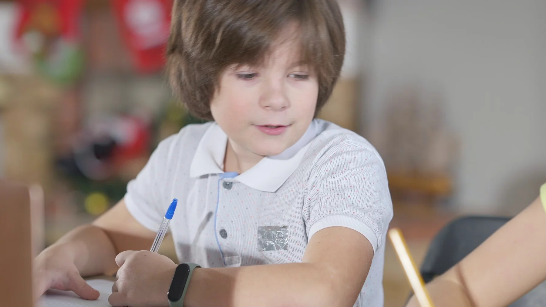 Na zdjęciu chłopiec siedzi w ławce w szkole i pisze coś na kartce