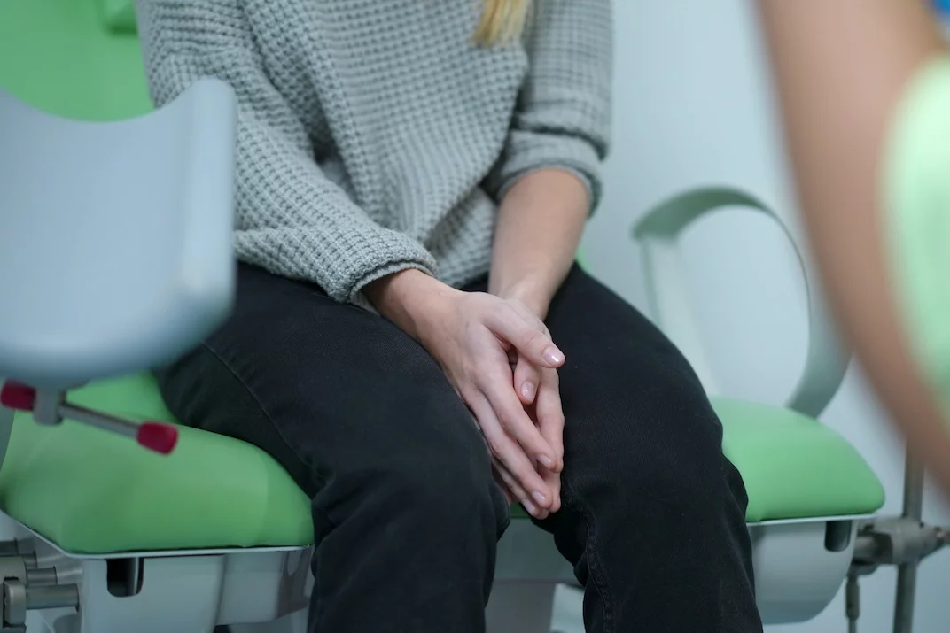 Pierwsza wizyta u ginekologa – jak powinna przebiegać Na zdjęciu widać nastolatkę siedzącą na fotelu ginekologicznym i wyraźnie zestresowaną