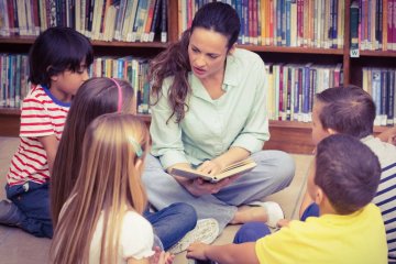 Nauczycielka języka polskiego czyta uczniom książkę w bibliotece.
