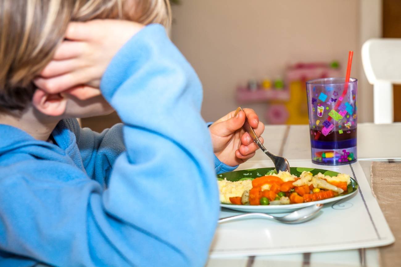 Dziecko patrzy z rezygnacją na talerz z obiadem.