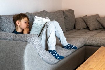 Chłopiec uczy się, siedząc z zeszytem na kanapie. Chłopiec uczy się, siedząc z zeszytem na kanapie.