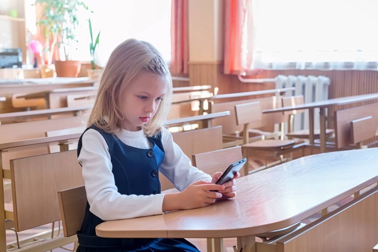 Uczennica siedzi w ławce i pisze wiadomość na smartfonie.