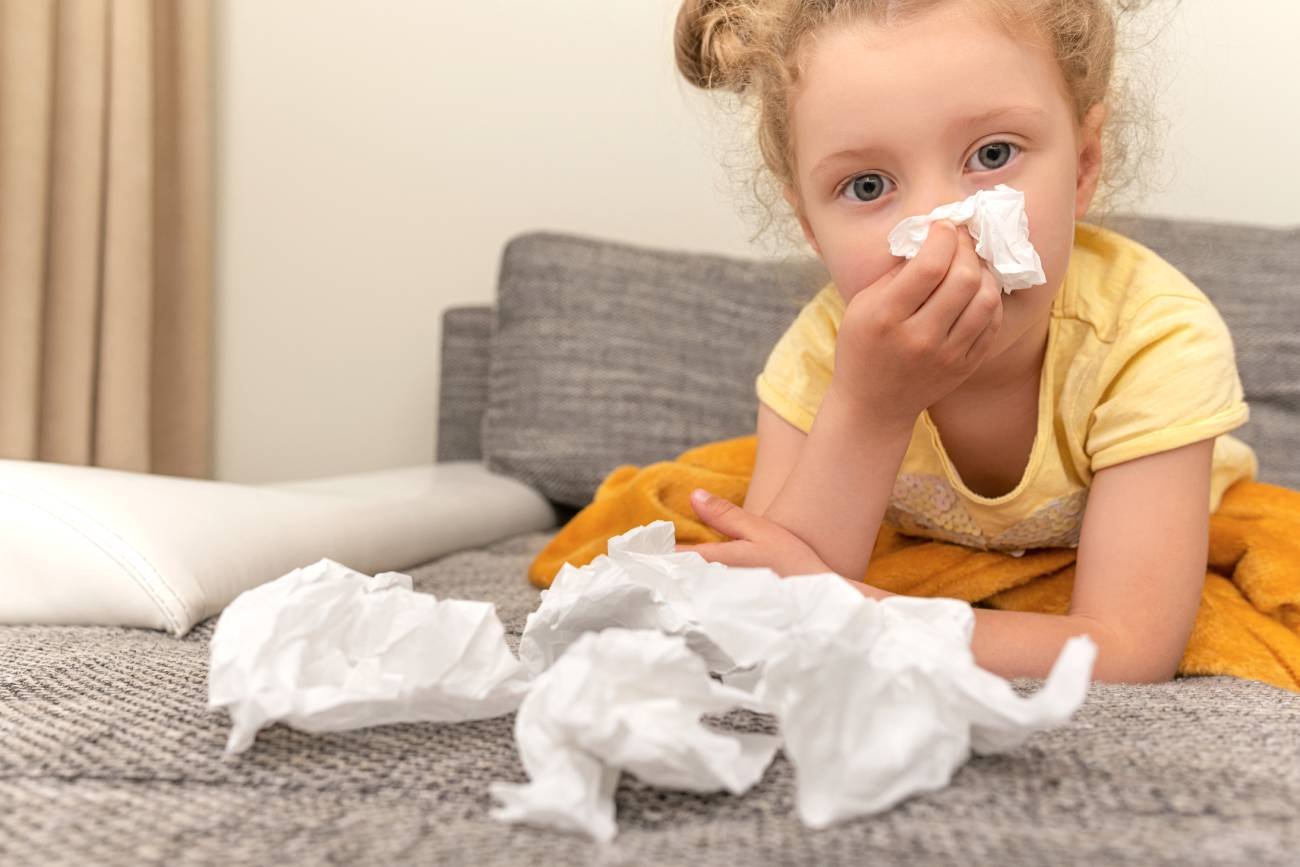 Dziewczynka w wieku przedszkolnym ma katar i dmucha nos w chusteczki.