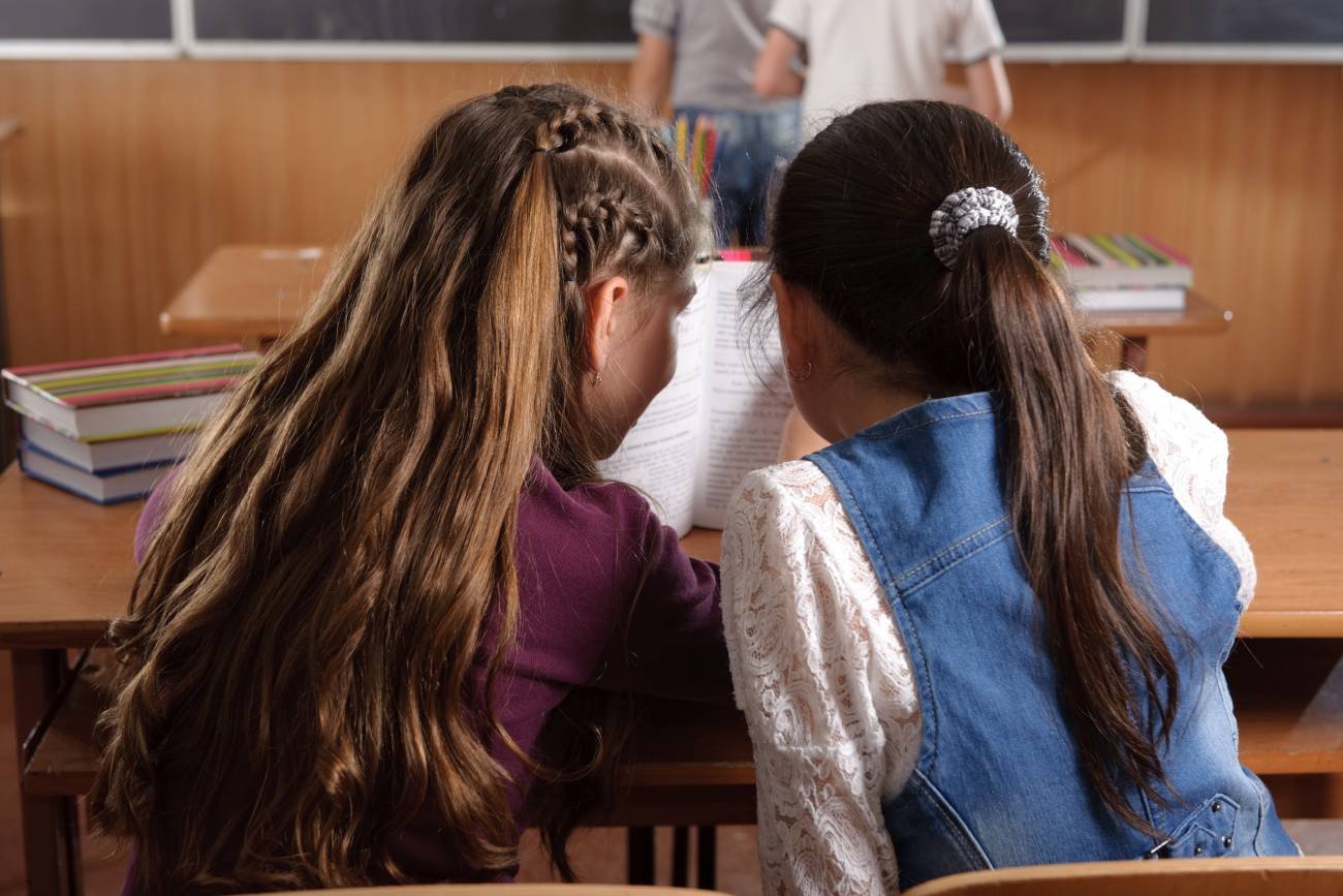 Dwie dziewczynki rozmawiają między sobą w ławce na lekcji.