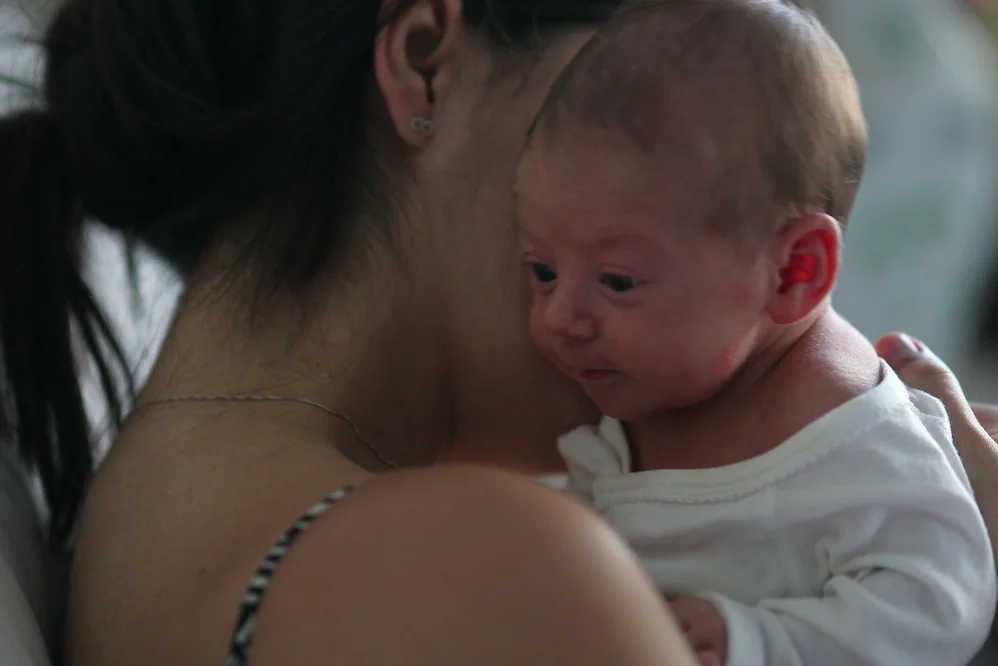 Dlaczego młoda mama może nie chcieć odwiedzin po porodzie Na zdjęciu widać młodą kobietę przytulającą noworodka.