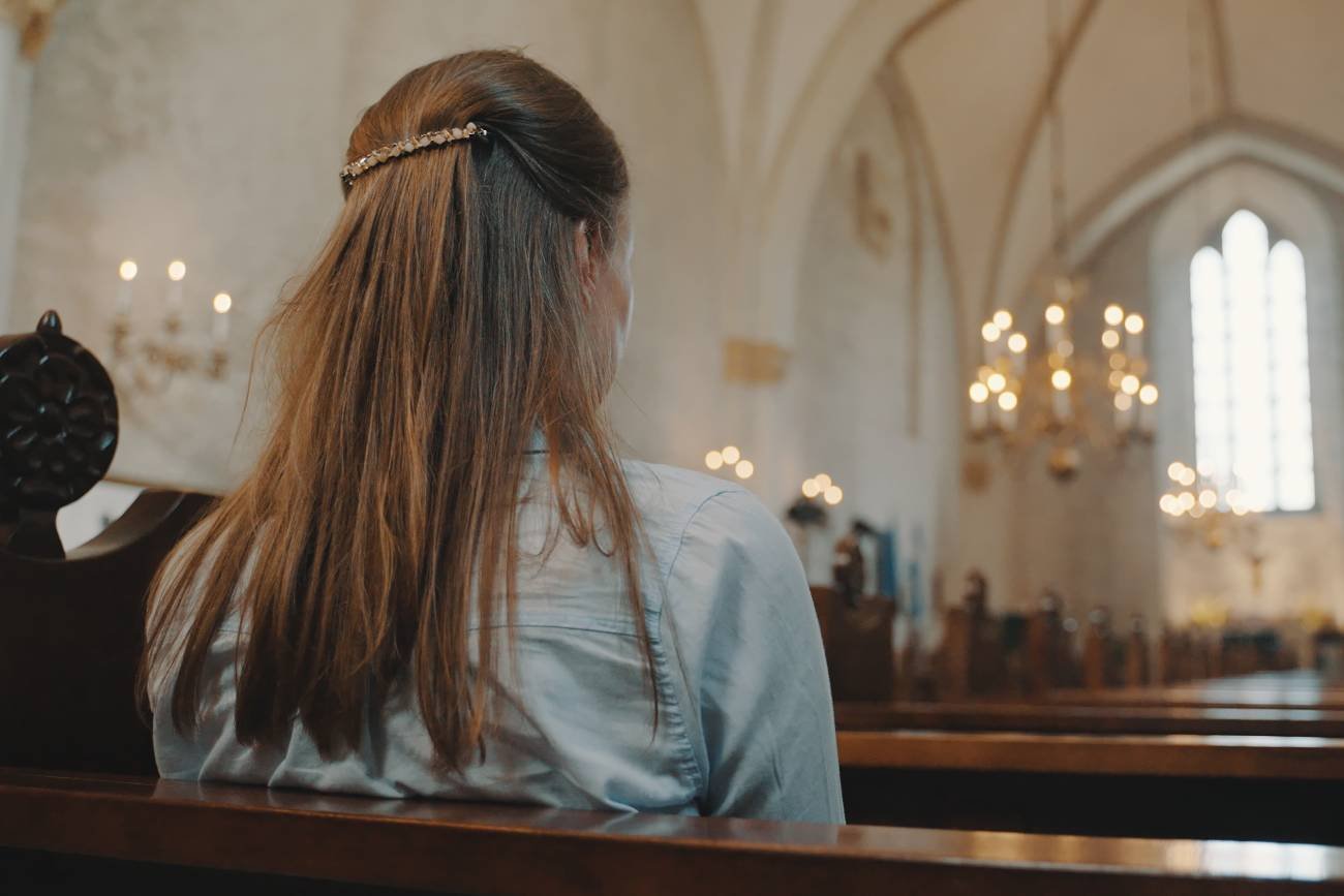 Uczennica w kościele siedzi w ławce.