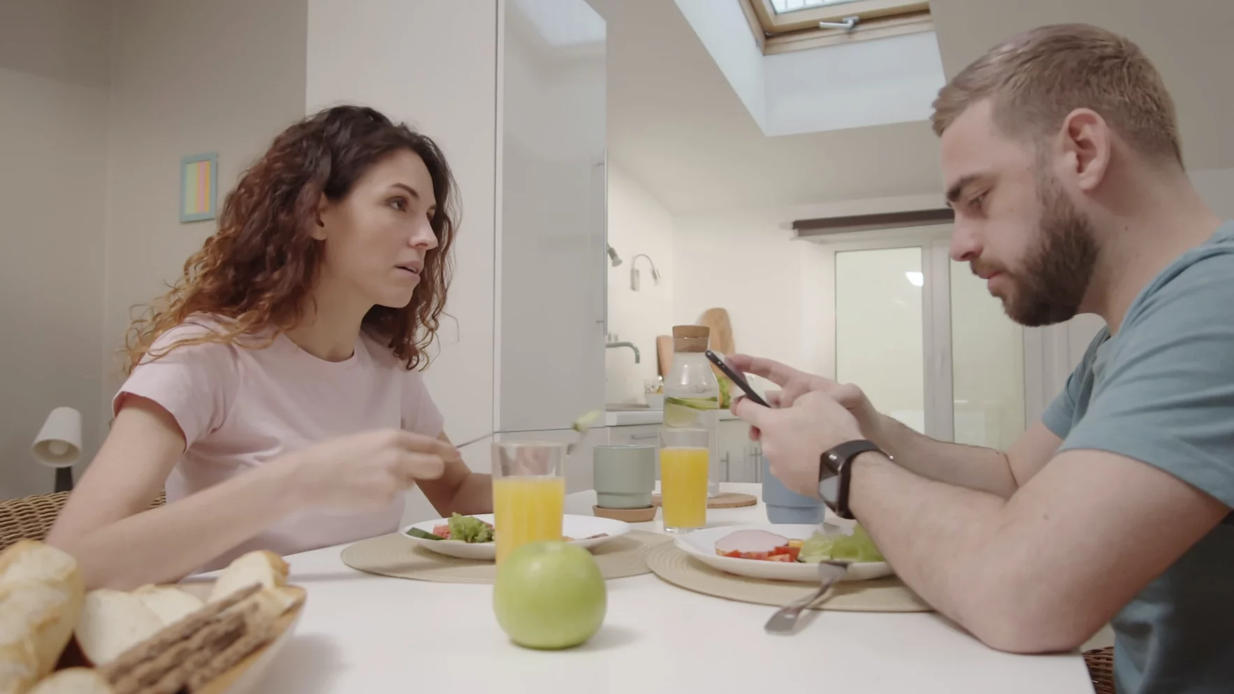 Kobieta i mężczyzna siedzą przy stole. Mężczyzna sprawdza coś w telefonie.