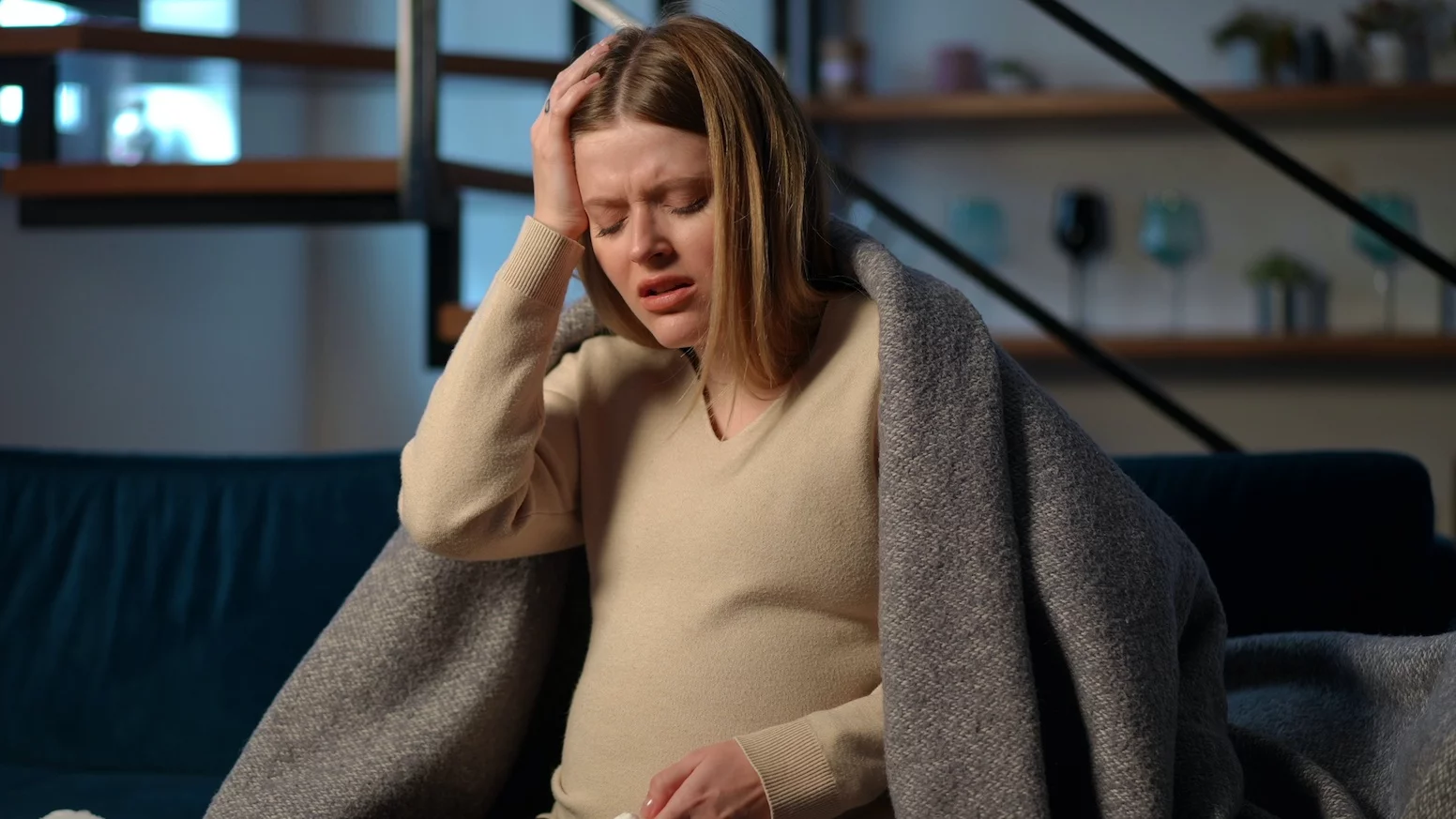 Dlaczego zapachy w ciąży są tak uciążliwe. Na zdjęciu ciężarna siedzi na kanapie z miną zniesmaczoną.